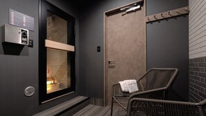 A modern bathroom with a steam shower, a wooden bench, and a wicker chair.