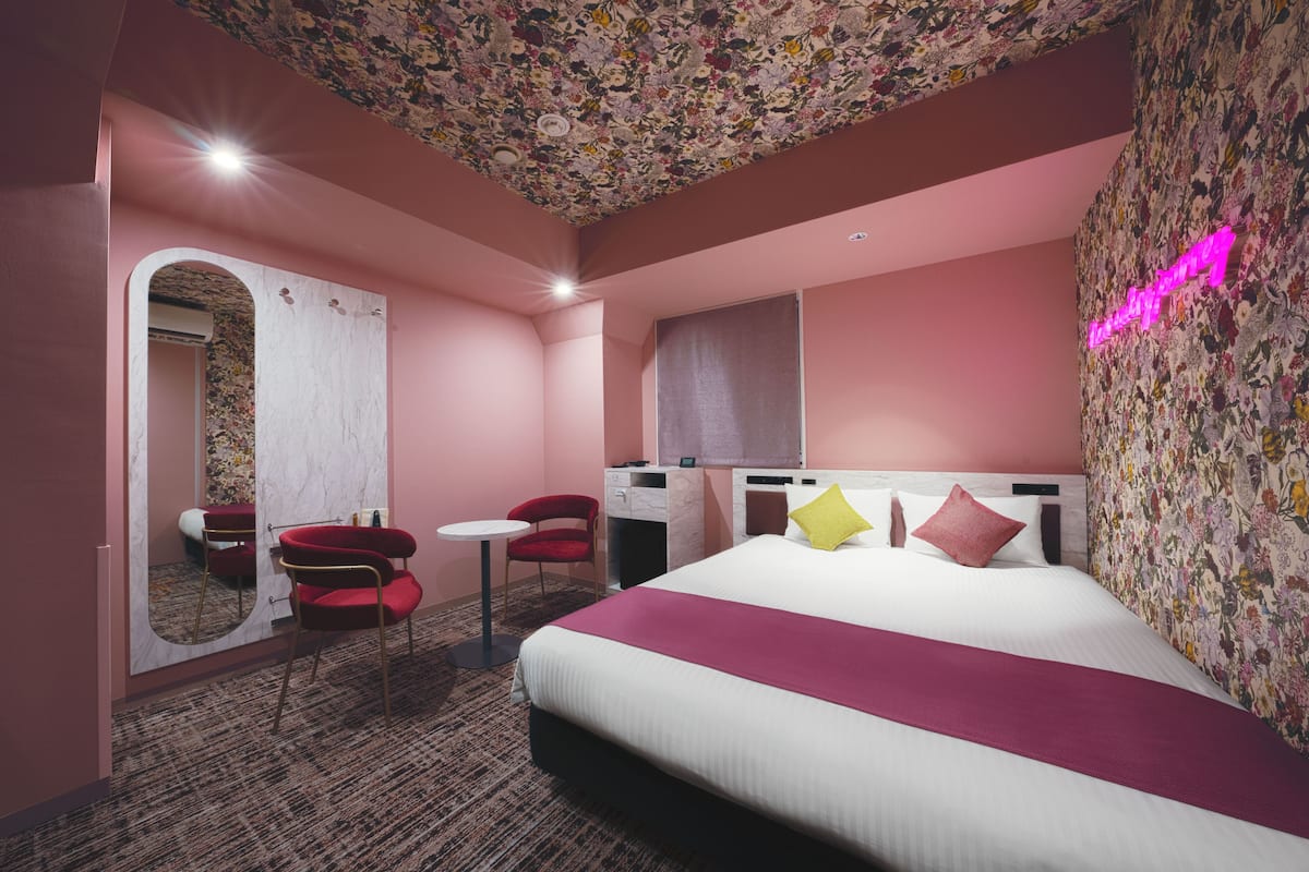 A hotel room with a large bed, a desk, a chair, a small table, and a mirror.