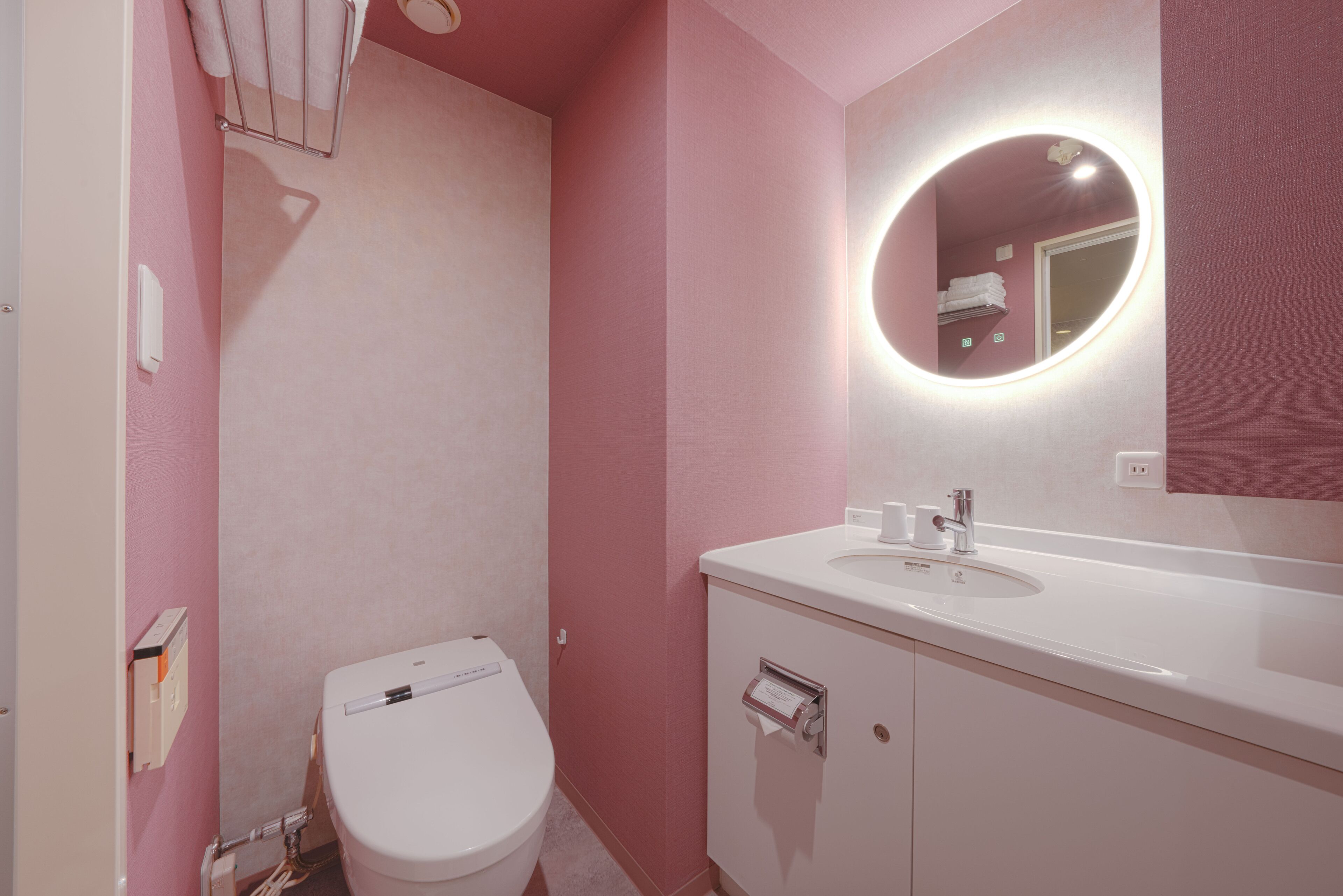 Un baño con inodoro blanco, lavamanos con espejo y paredes rosadas.