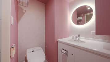 Un baño con inodoro blanco, lavamanos con espejo y paredes rosadas.
