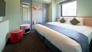 A hotel room with a large bed, a round red ottoman, a bathroom with a mirror and towel rack, and a window with a view.