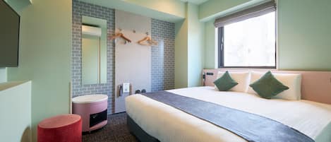 Une chambre d’hôtel avec un grand lit, un pouf rond rouge, une salle de bain avec un miroir et un porte-serviettes, et une fenêtre donnant sur un paysage agréable.