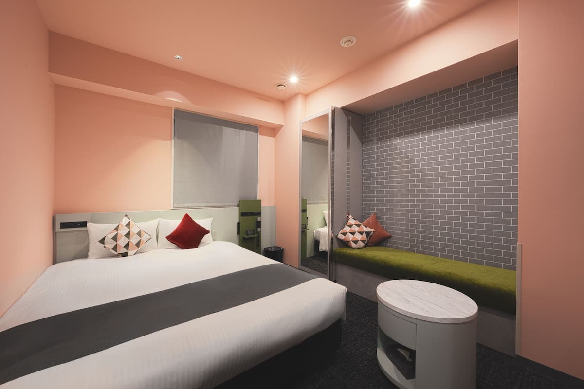 A modern hotel room with a large bed, a small round table, a mirror, and a brick-patterned wall.