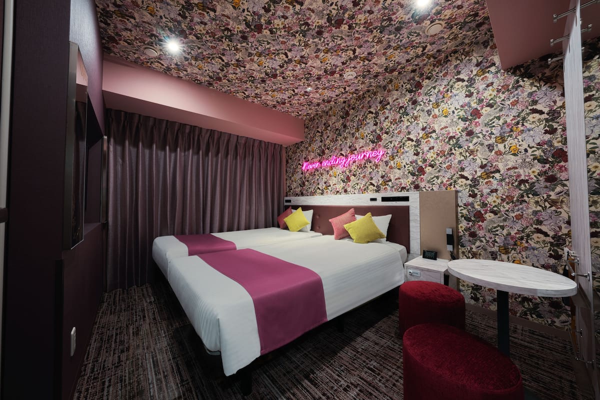 A hotel room with a floral-patterned ceiling, a bed with white and pink bedding, a small round table, and a red ottoman.