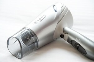 A portable hair dryer with a transparent water-resistant section, a silver body, and a control button.