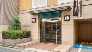 The entrance to Villa Fontaine hotel with a glass door, a small garden, and a tiled facade. - Hotel Villa Fontaine Tokyo - Jimbocho (Tokyo)