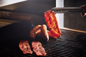 A grill with sausages and steaks being cooked.