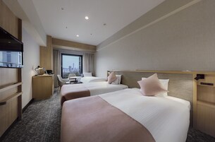 A hotel room with two beds, a desk, a chair, and a TV.