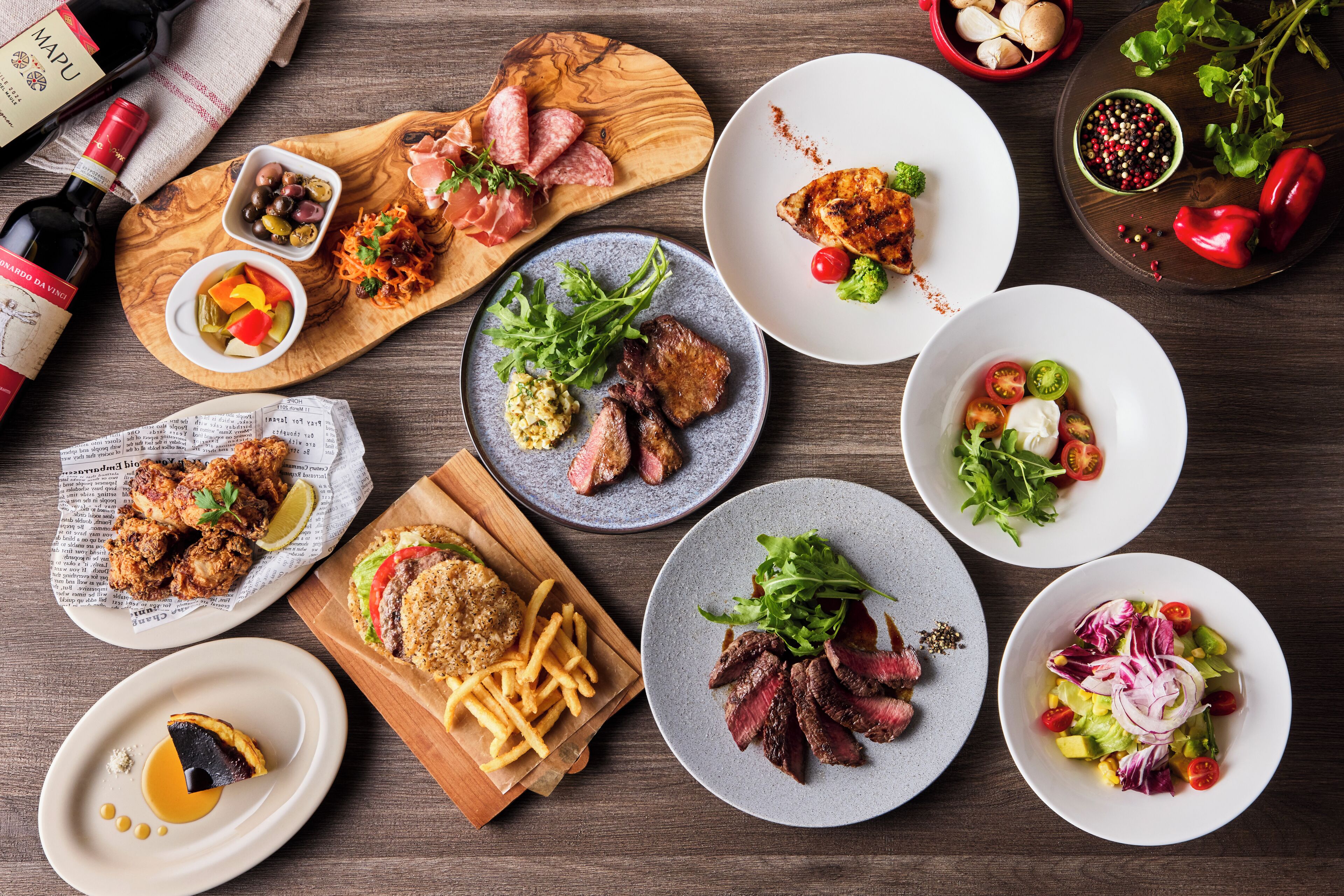 Une variété de plats, notamment des steaks, des frites et des salades, disposés sur une table en bois.