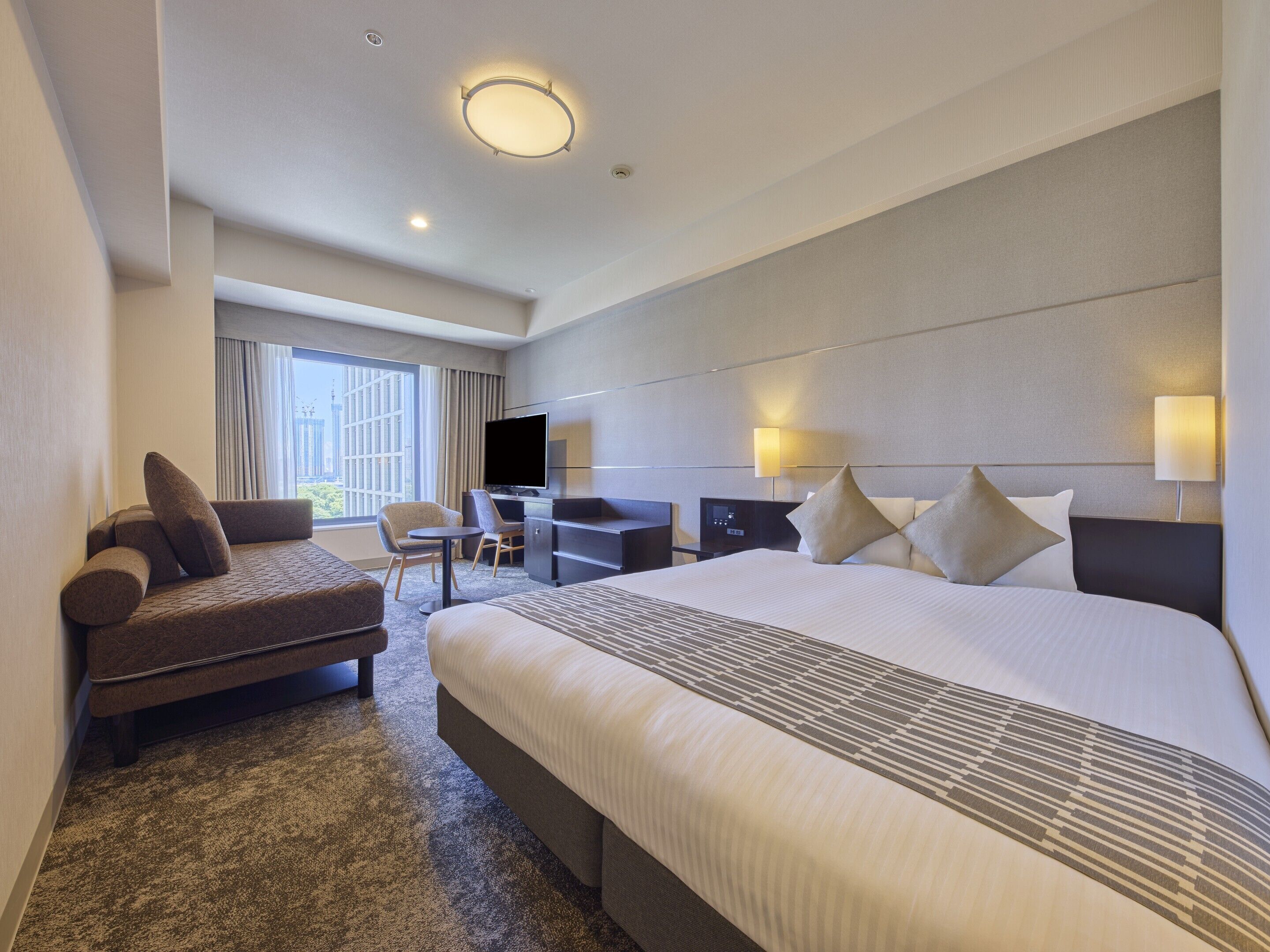 A hotel room with a large bed, a desk, a chair, and a television.