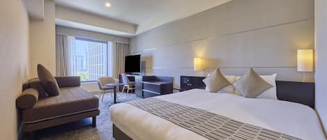 A hotel room with a large bed, a desk, a chair, and a television.