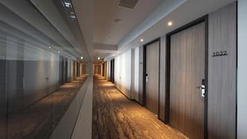 A hotel corridor with a carpeted floor, wooden doors, and a number sign on one door.