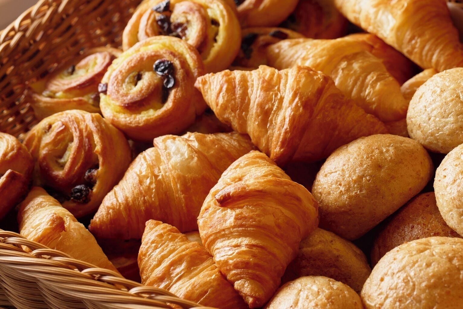 Un panier rempli de différents types de viennoiseries, notamment des croissants et des pains au lait.