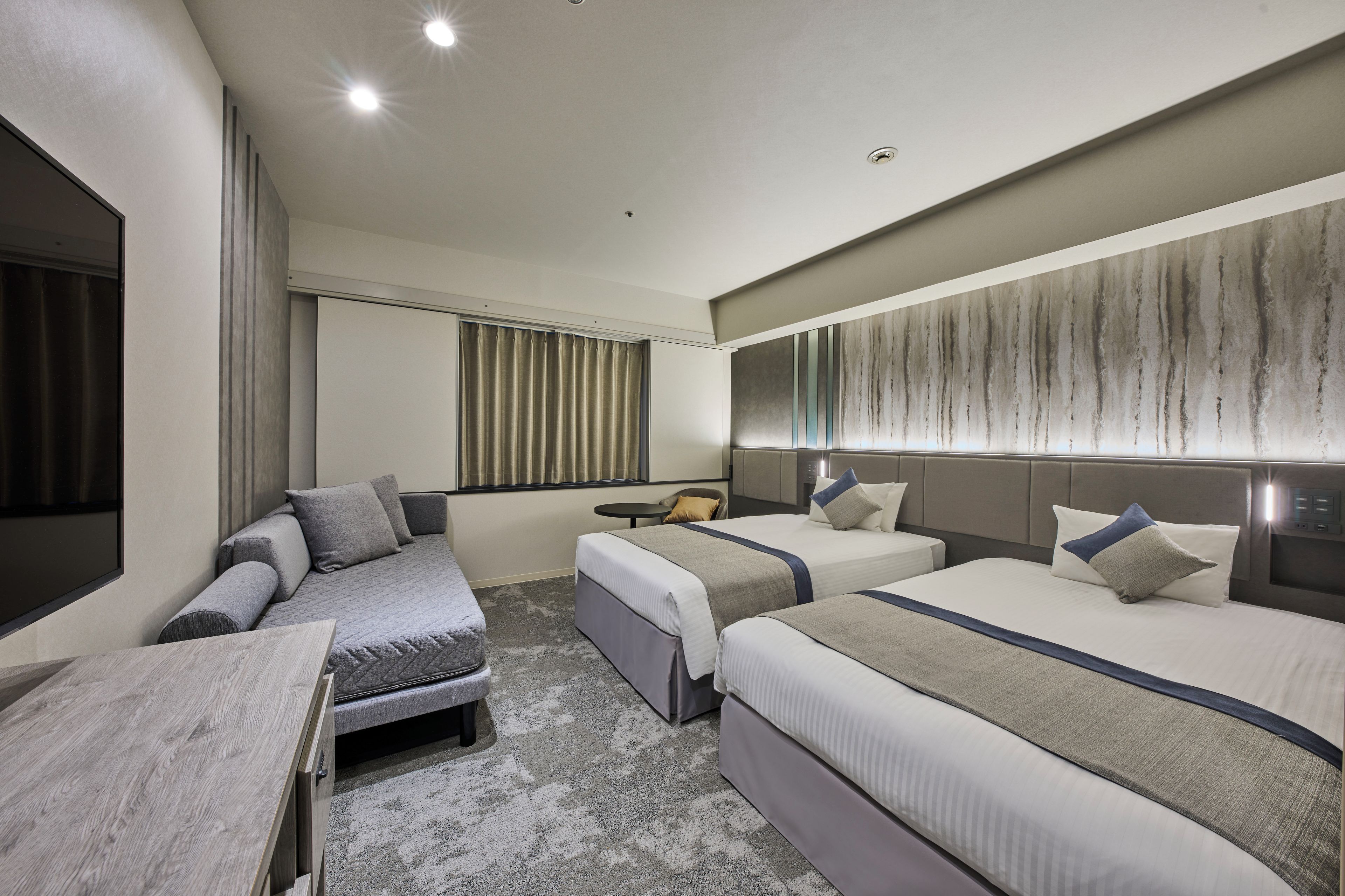 Una habitación de hotel moderna con dos camas, un sofá, una mesita y un espejo grande.