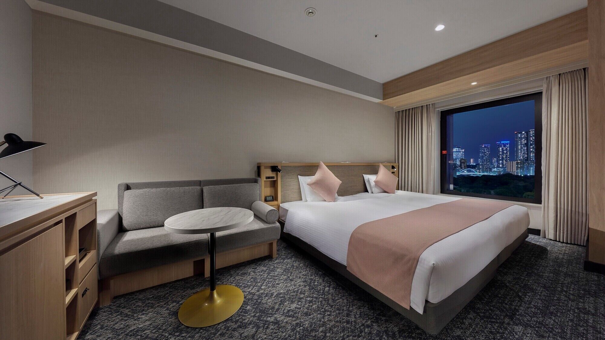 Une chambre d’hôtel avec un lit, un canapé, un bureau et une vue sur le paysage urbain la nuit.