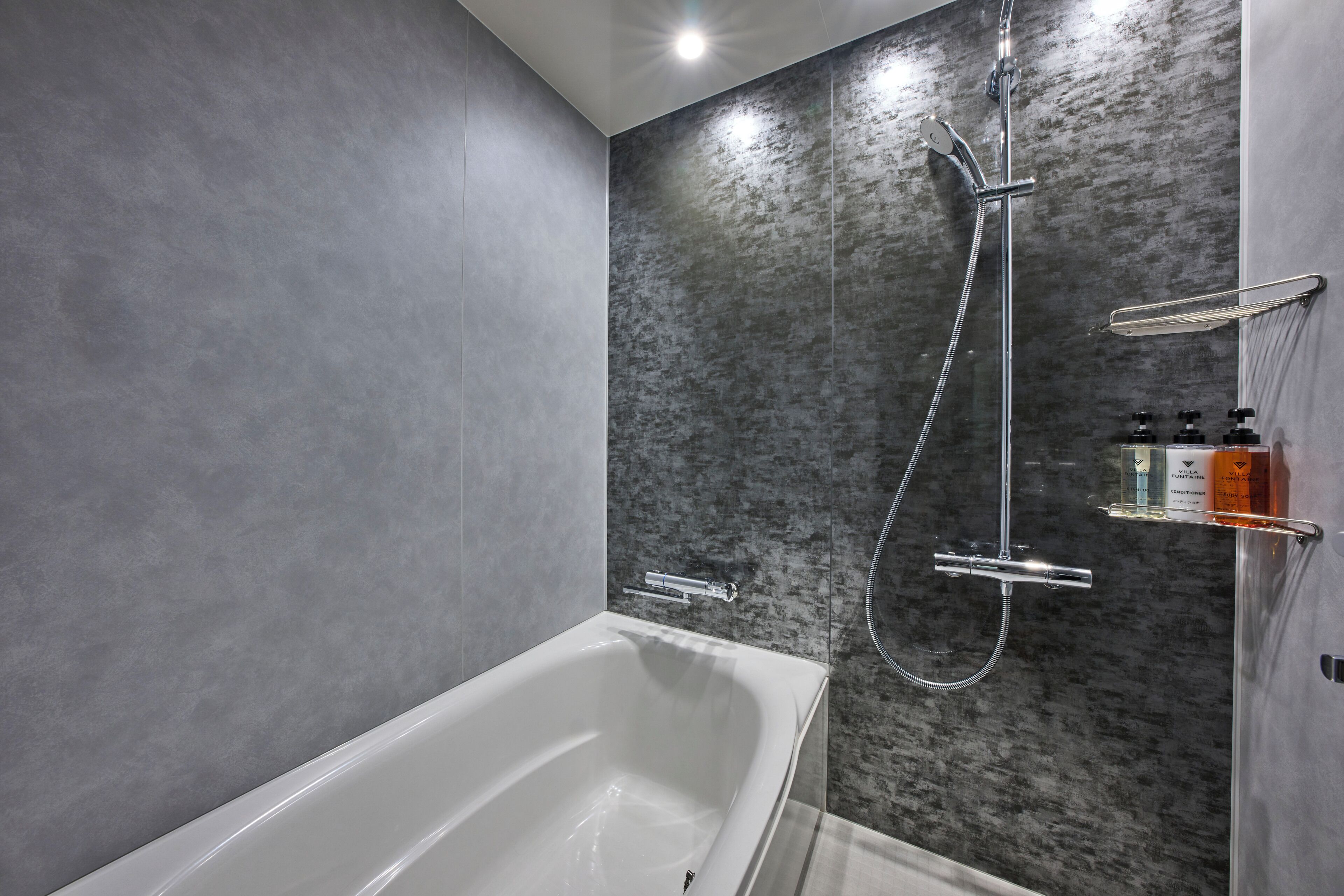 A modern bathroom with a white bathtub, a shower with a handheld showerhead, and a glass shelf with toiletries.