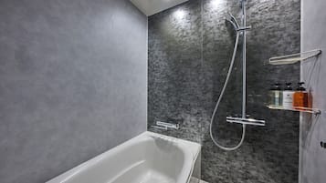 Un baño moderno con una bañera blanca, ducha con cabezal de ducha manual y un estante de vidrio con artículos de aseo.