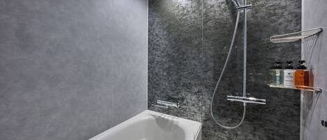 A modern bathroom with a white bathtub, a shower with a handheld showerhead, and a glass shelf with toiletries.