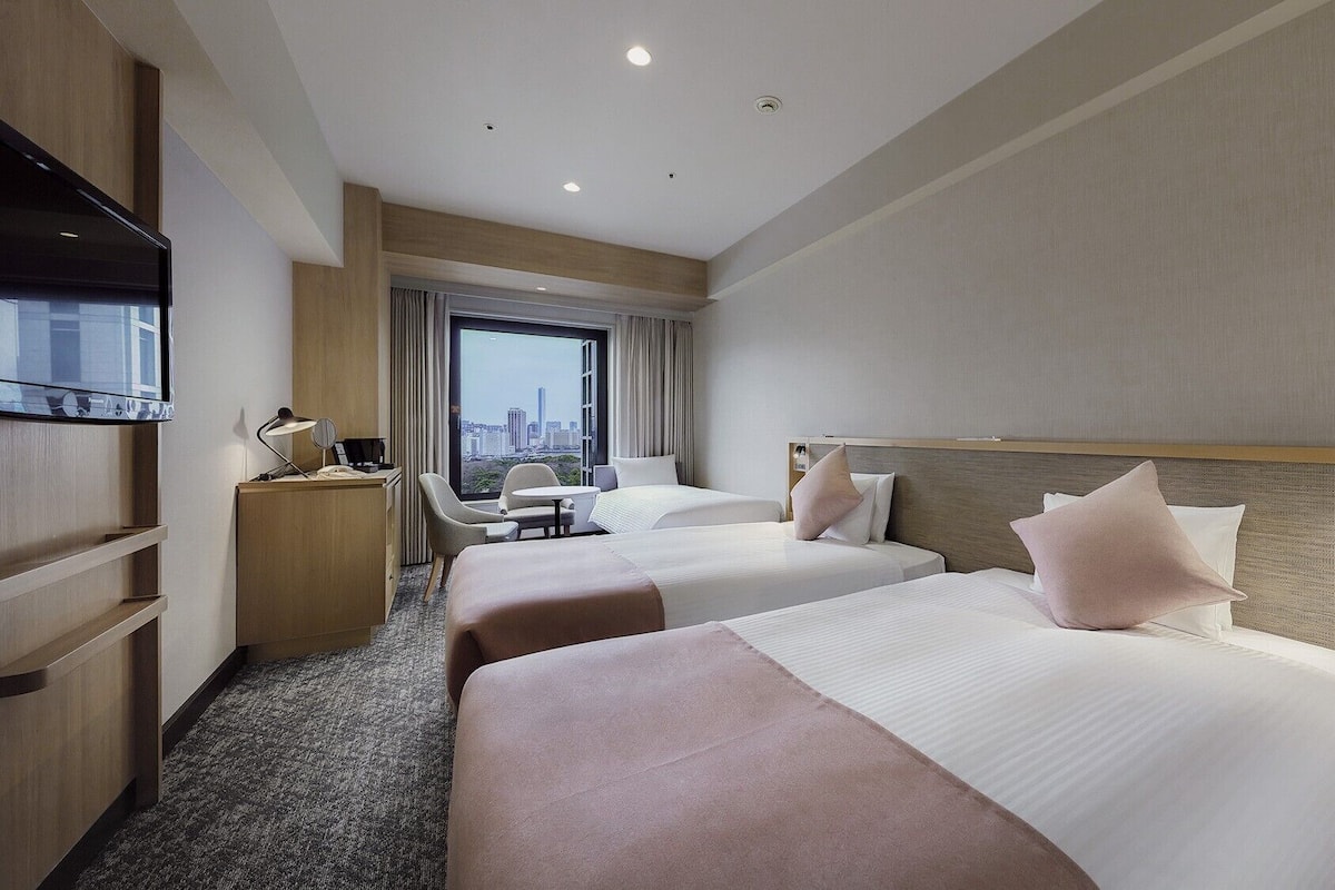 Quarto de hotel com duas camas, uma mesa, uma cadeira e uma televisão.