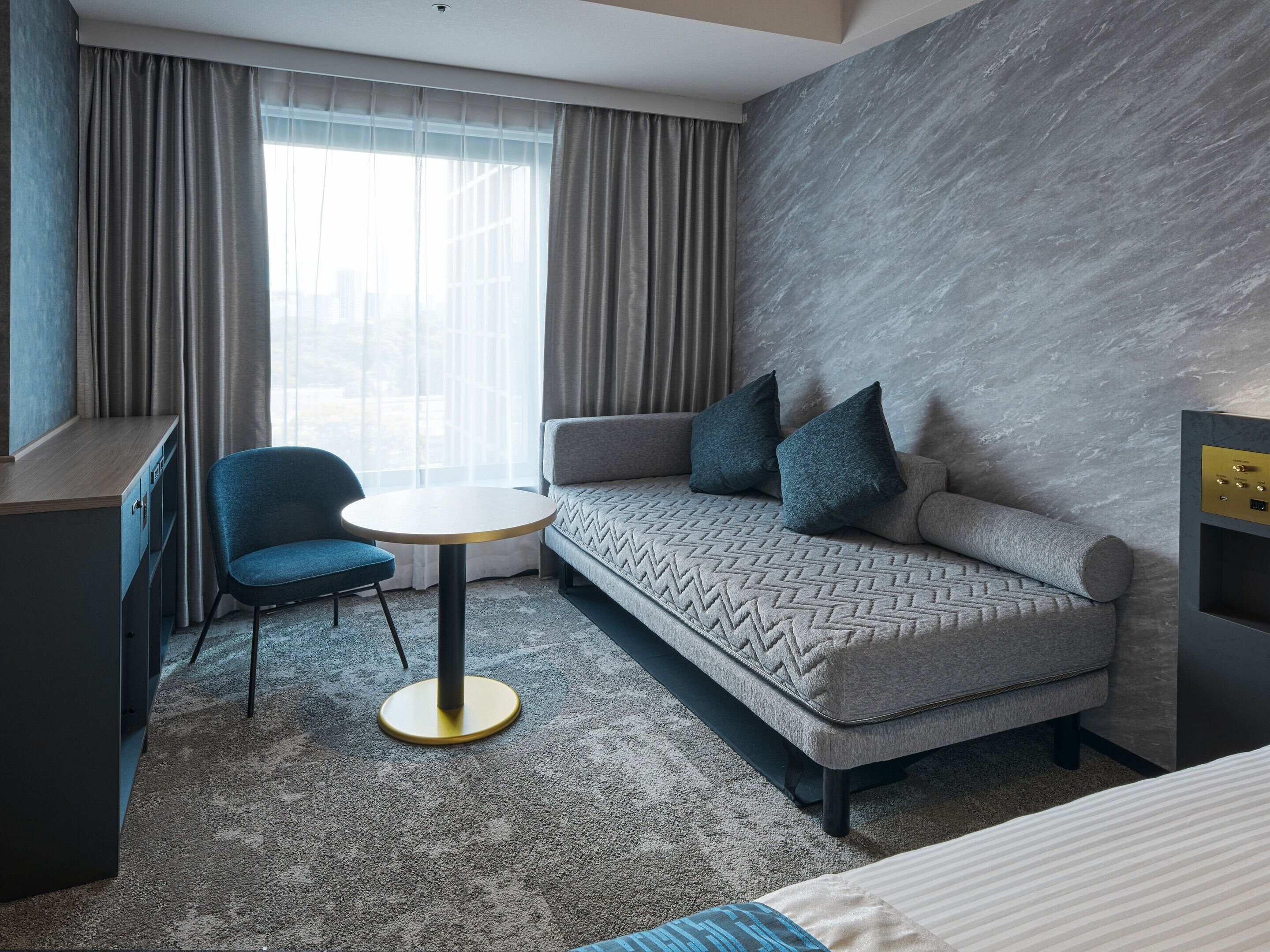 A modern hotel room with a sofa, a chair, a small round table, and a desk.