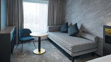 A modern hotel room with a sofa, a chair, a small round table, and a desk.