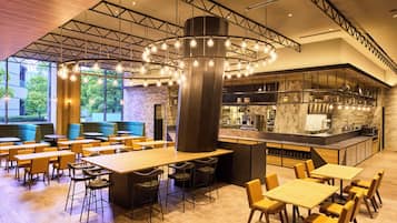 A modern restaurant with high ceilings, exposed beams, and a central light fixture. Tables and booths are arranged for dining.
