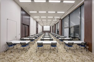 A conference room with rows of tables and chairs, large windows, and a carpeted floor.