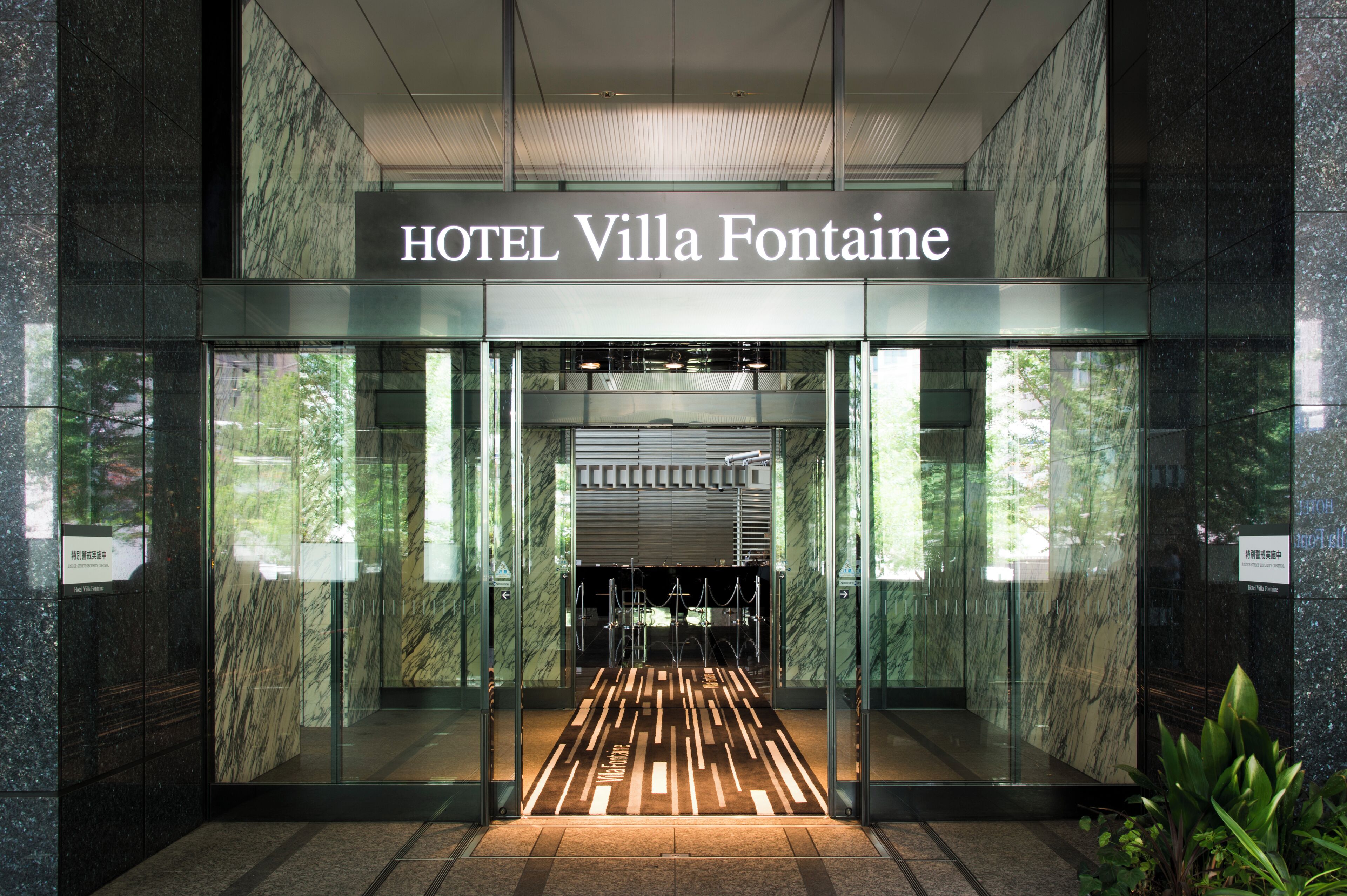 La entrada del HOTEL Villa Fontaine, con una fachada moderna de vidrio, un interior de mármol y un área de recepción acogedora.