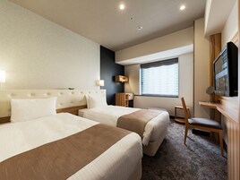 A hotel room with two beds, a desk, a chair, a TV, and a window with blinds.