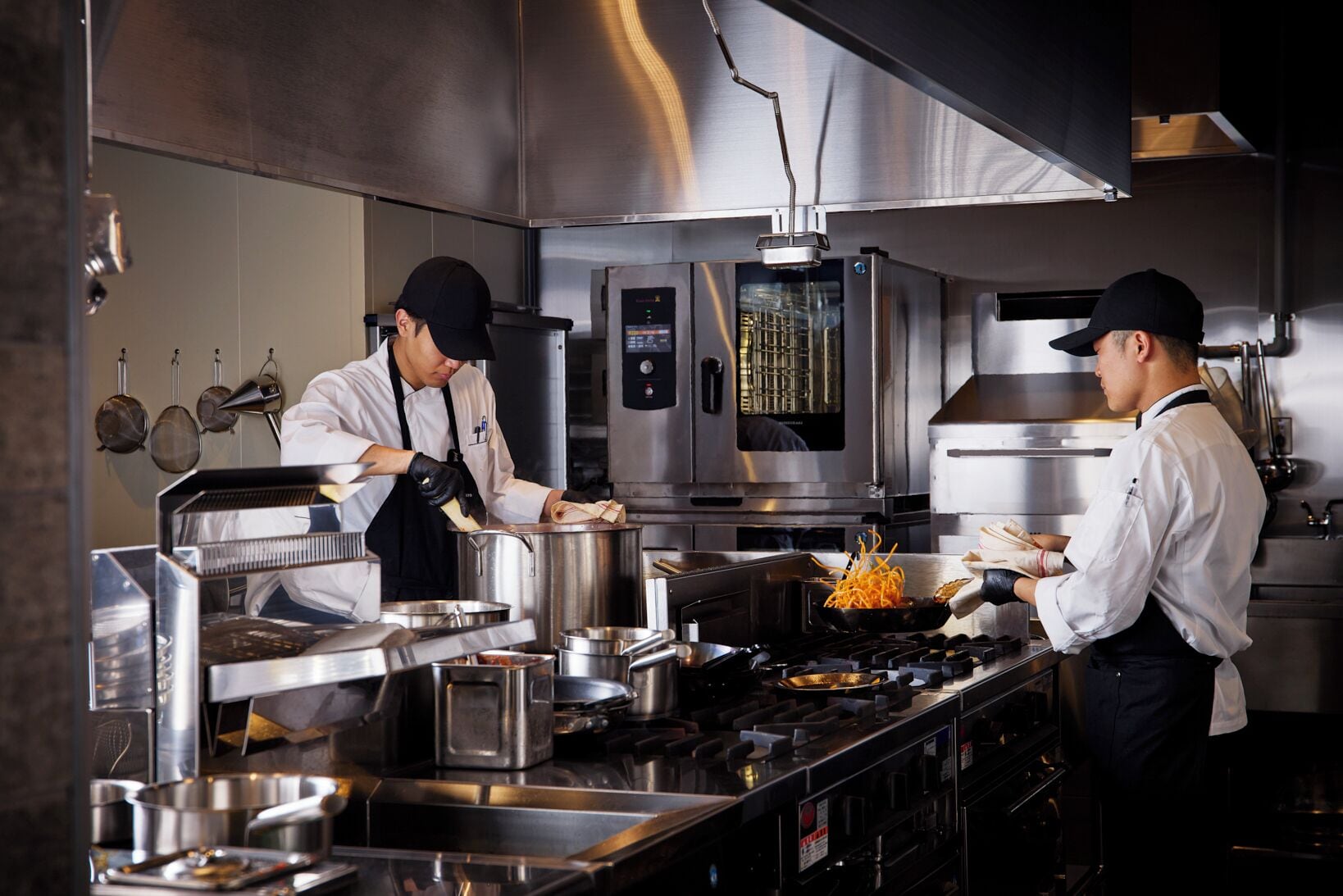 A professional kitchen with stainless steel appliances, a large oven, and chefs preparing food.