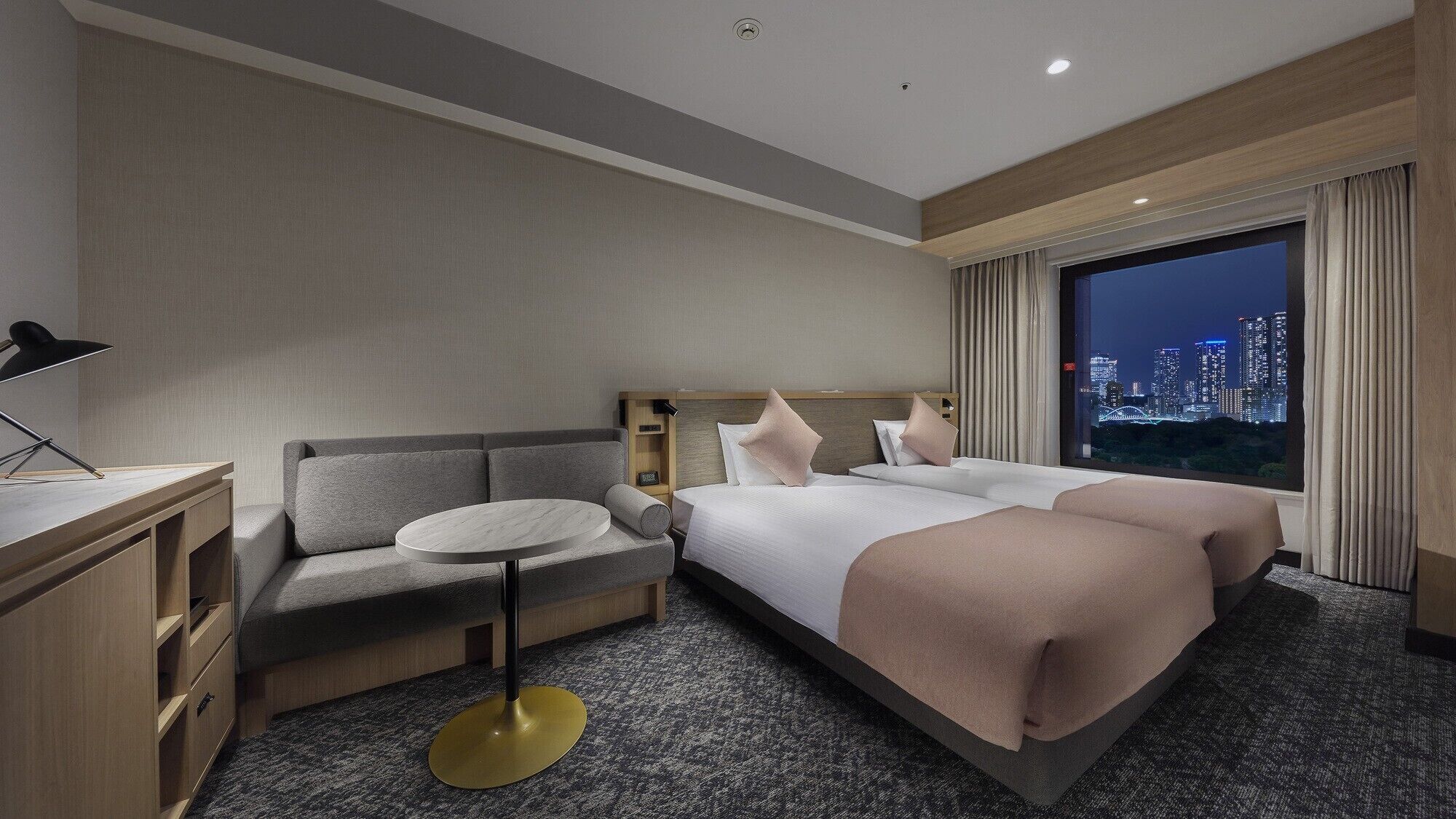 Une chambre d’hôtel avec un lit, un canapé, un bureau et une vue sur le paysage urbain illuminé la nuit.