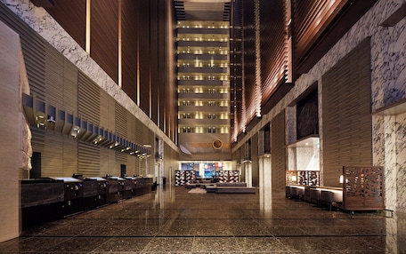 A spacious lobby with a long reception desk, seating area, and a high ceiling with lighting fixtures.