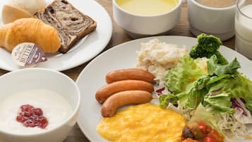 A breakfast plate with croissants, bread, sausages, scrambled eggs, and a salad.