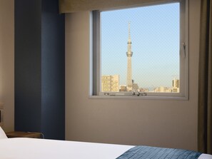 A hotel room with a large window offering a view of a tall tower and surrounding buildings. - Hotel Villa Fontaine Tokyo - Ueno Okachimachi (Tokyo)