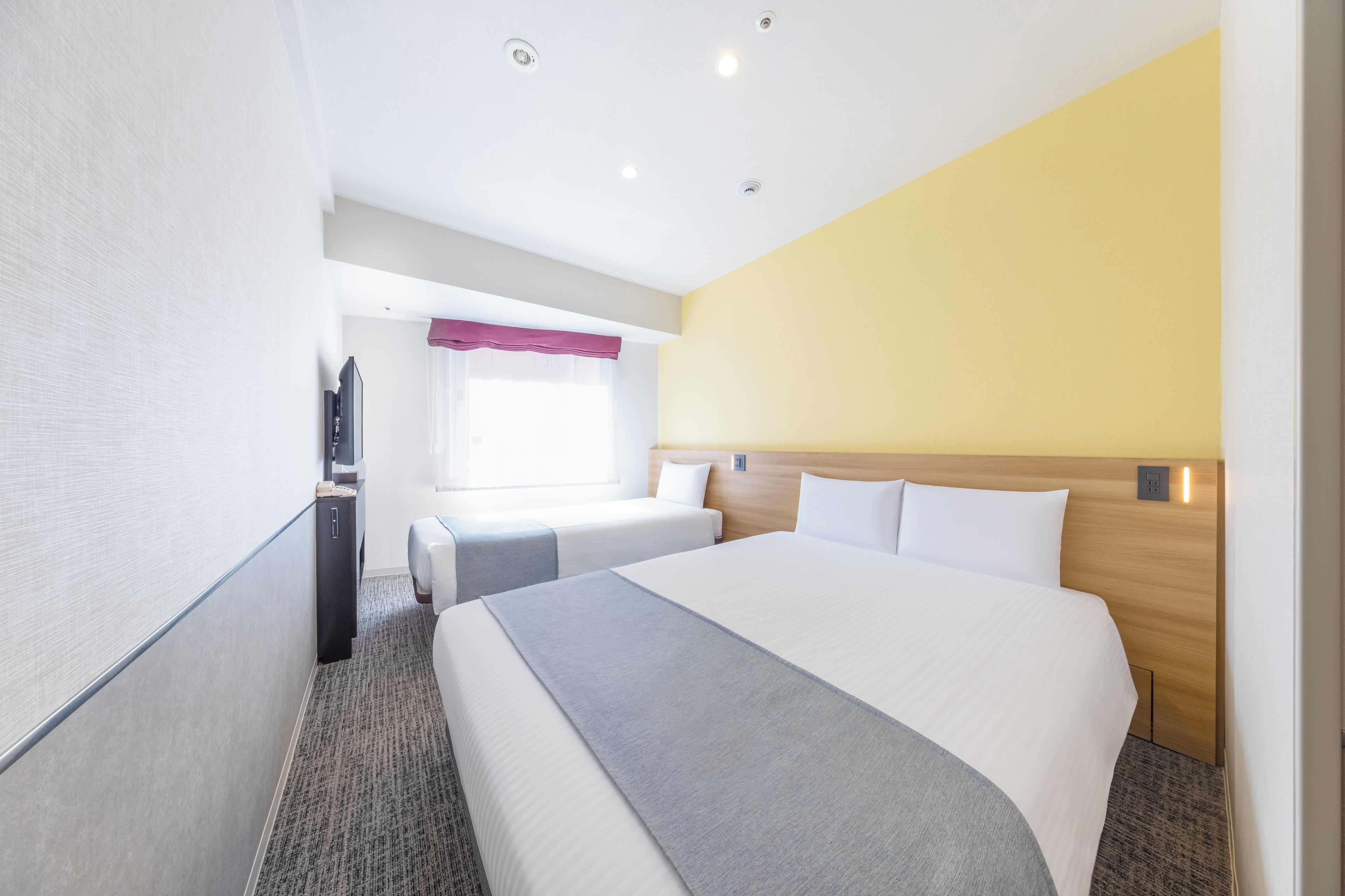 A hotel room with a large bed, two smaller beds, a desk with a telephone, and a television.