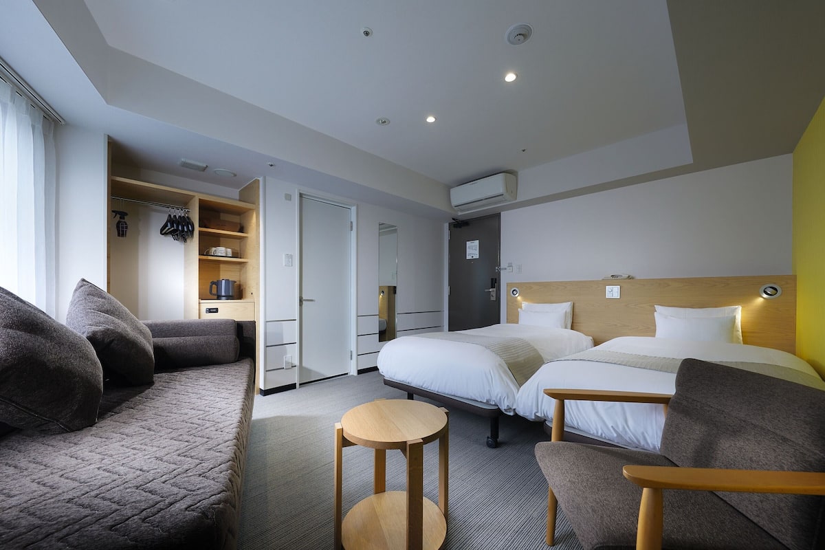 A hotel room with two beds, a sofa, a small round table, and a wardrobe.