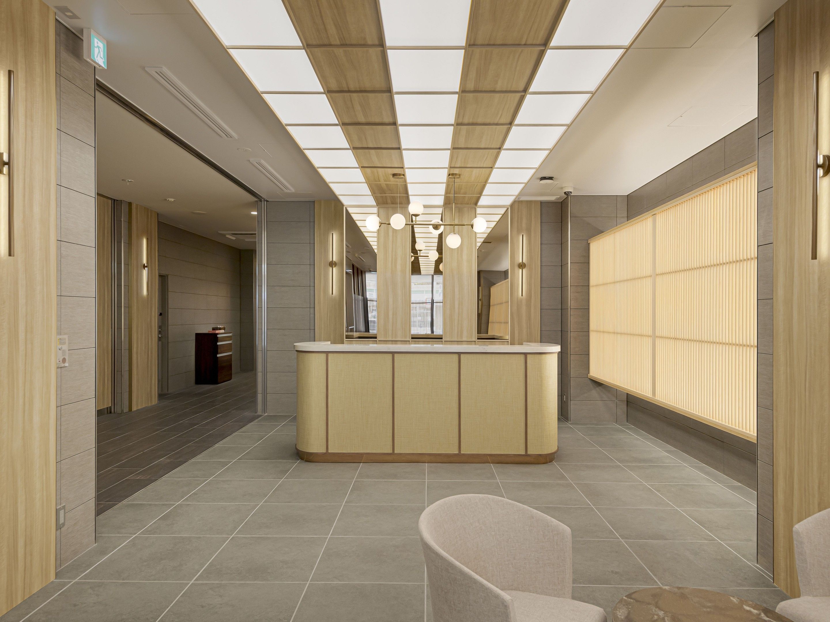 Un hall d’hôtel moderne avec un comptoir d’accueil central, un espace salon et une grande fenêtre équipée de stores.