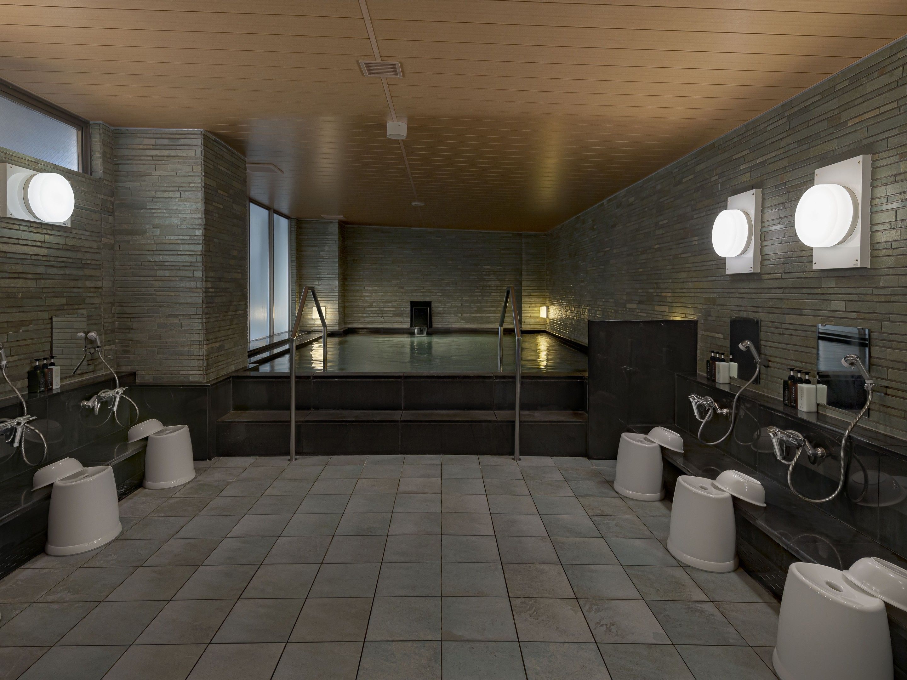 A modern bathroom with a large heated pool, multiple urinals, and a stone wall design.