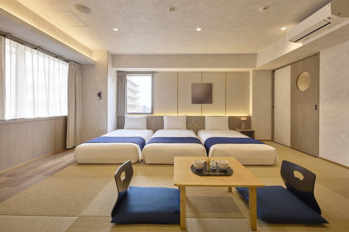 A hotel room with two beds, a small table with a tray, and a view of the city through the window.