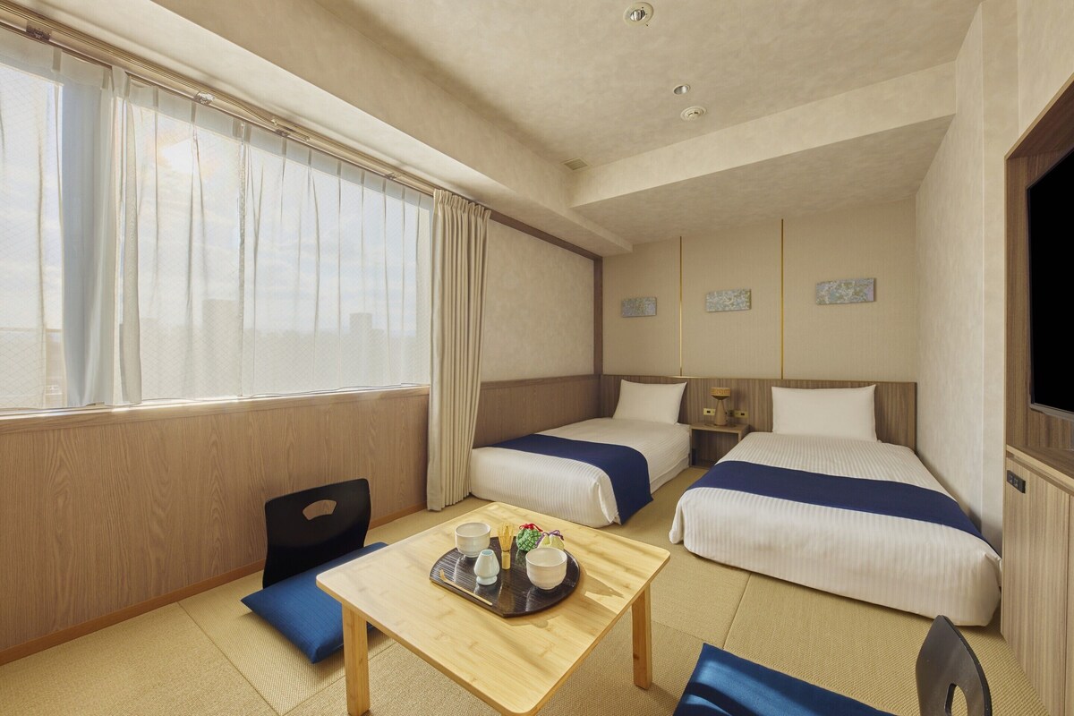 A hotel room with two beds, a small table with a tray of items, a chair, and a television.