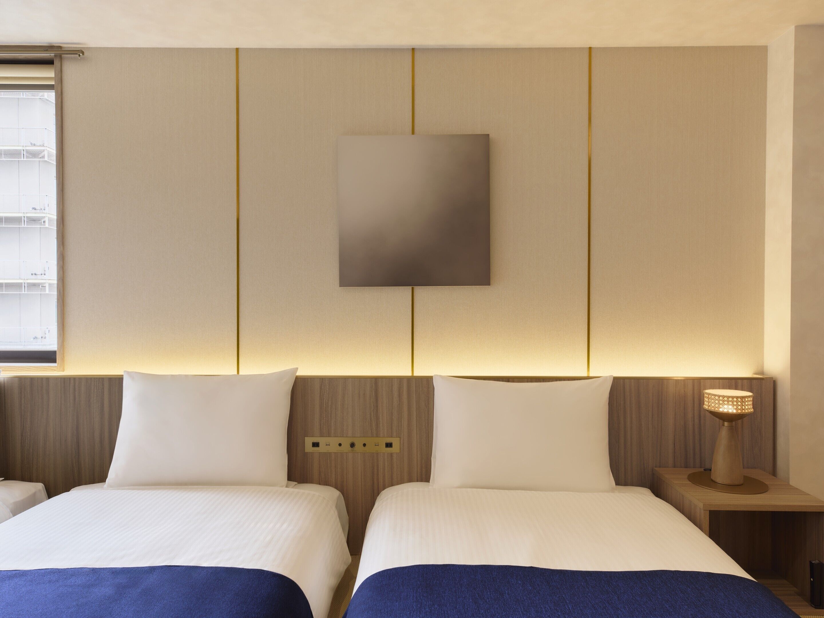 Hotellihuone, jossa on kaksi sänkyä, seinälle asennettu taulutelevisio ja yöpöytälamppu.