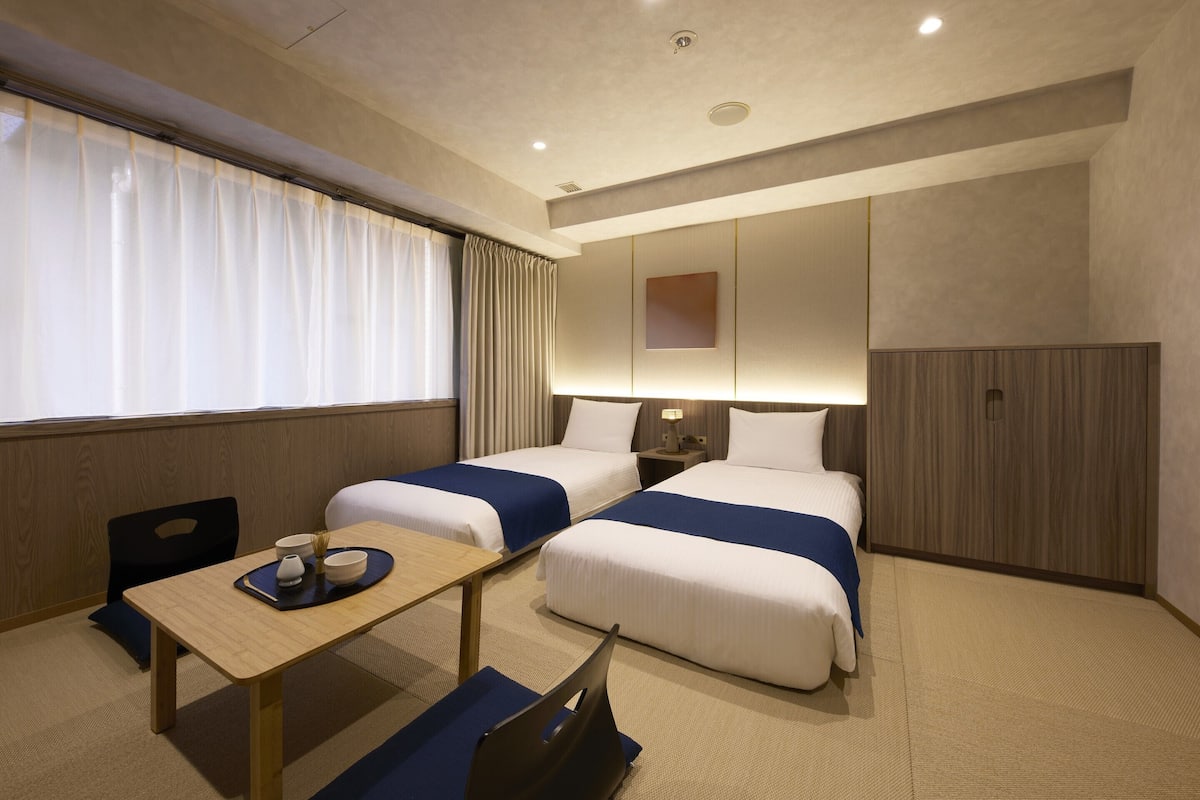 A hotel room with two beds, a small table, a chair, a desk, and a wardrobe.