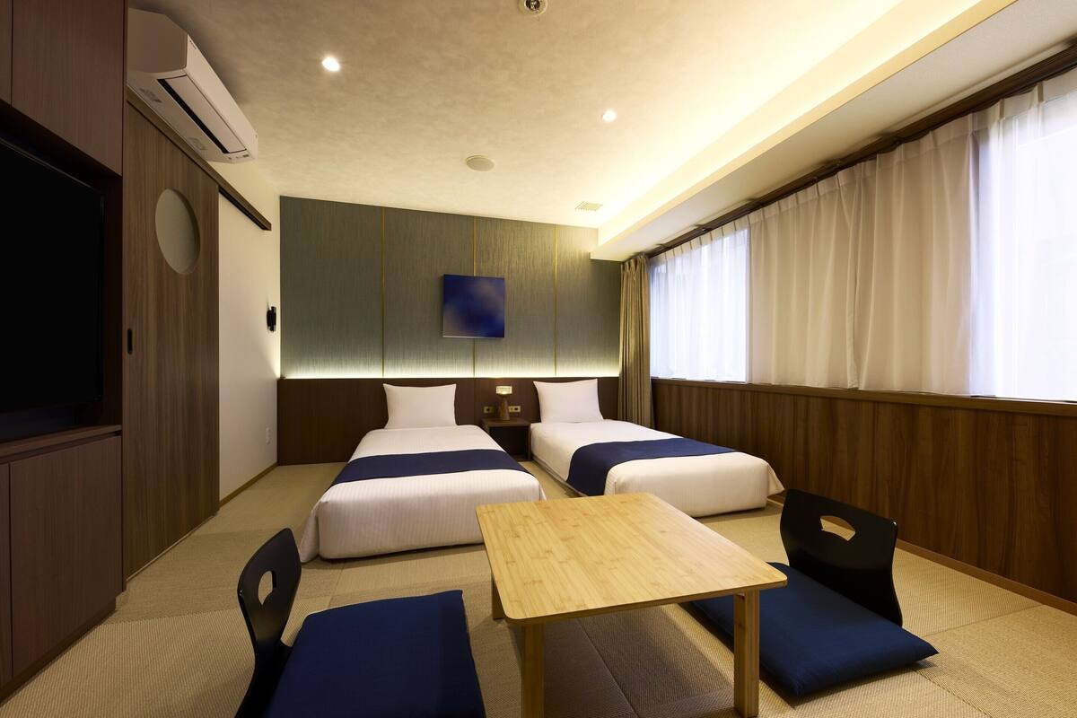 A hotel room with two beds, a TV, a wooden table, and a seating area.