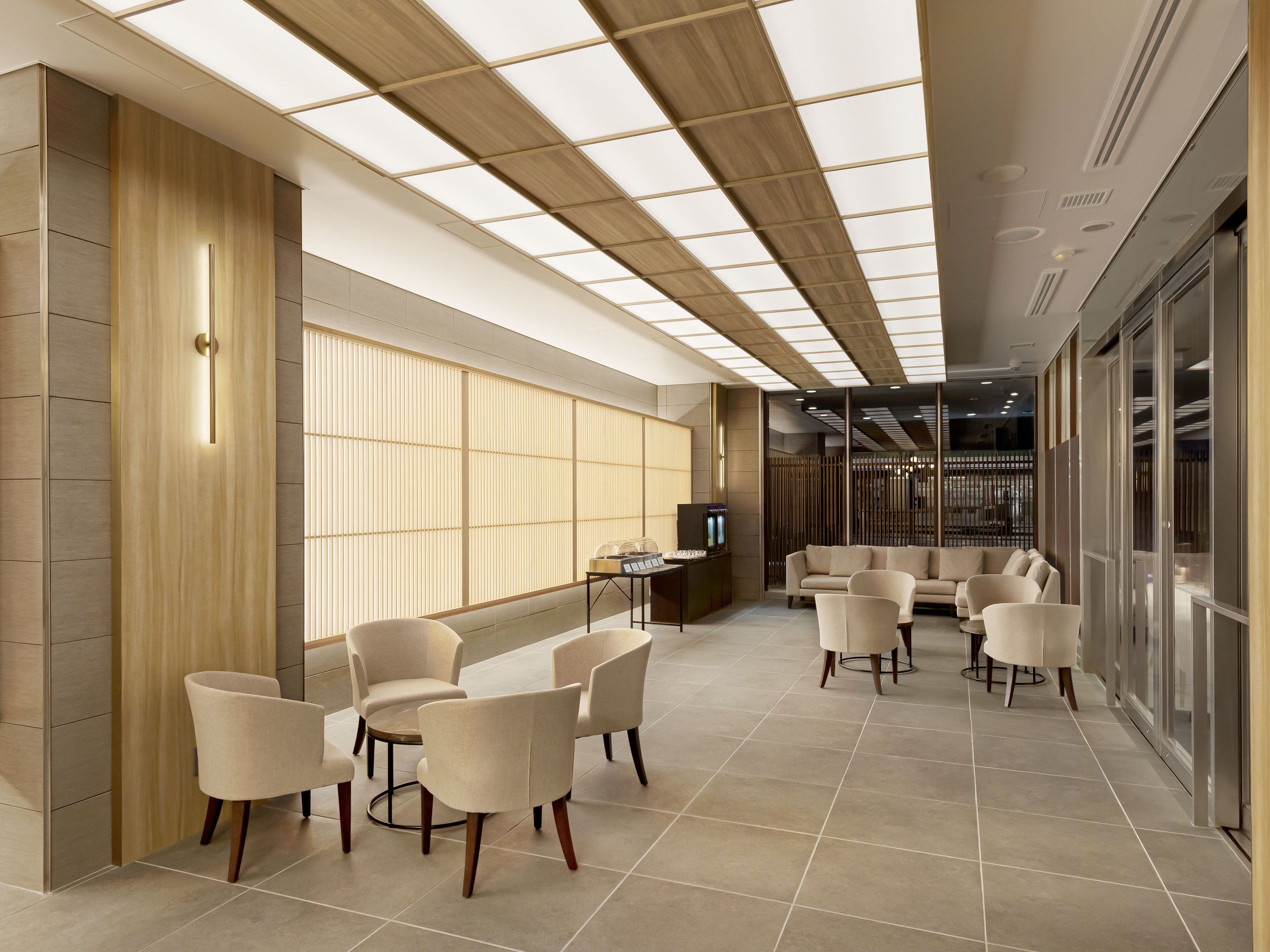 A modern hotel lobby with a seating area, a reception desk, and a large window.