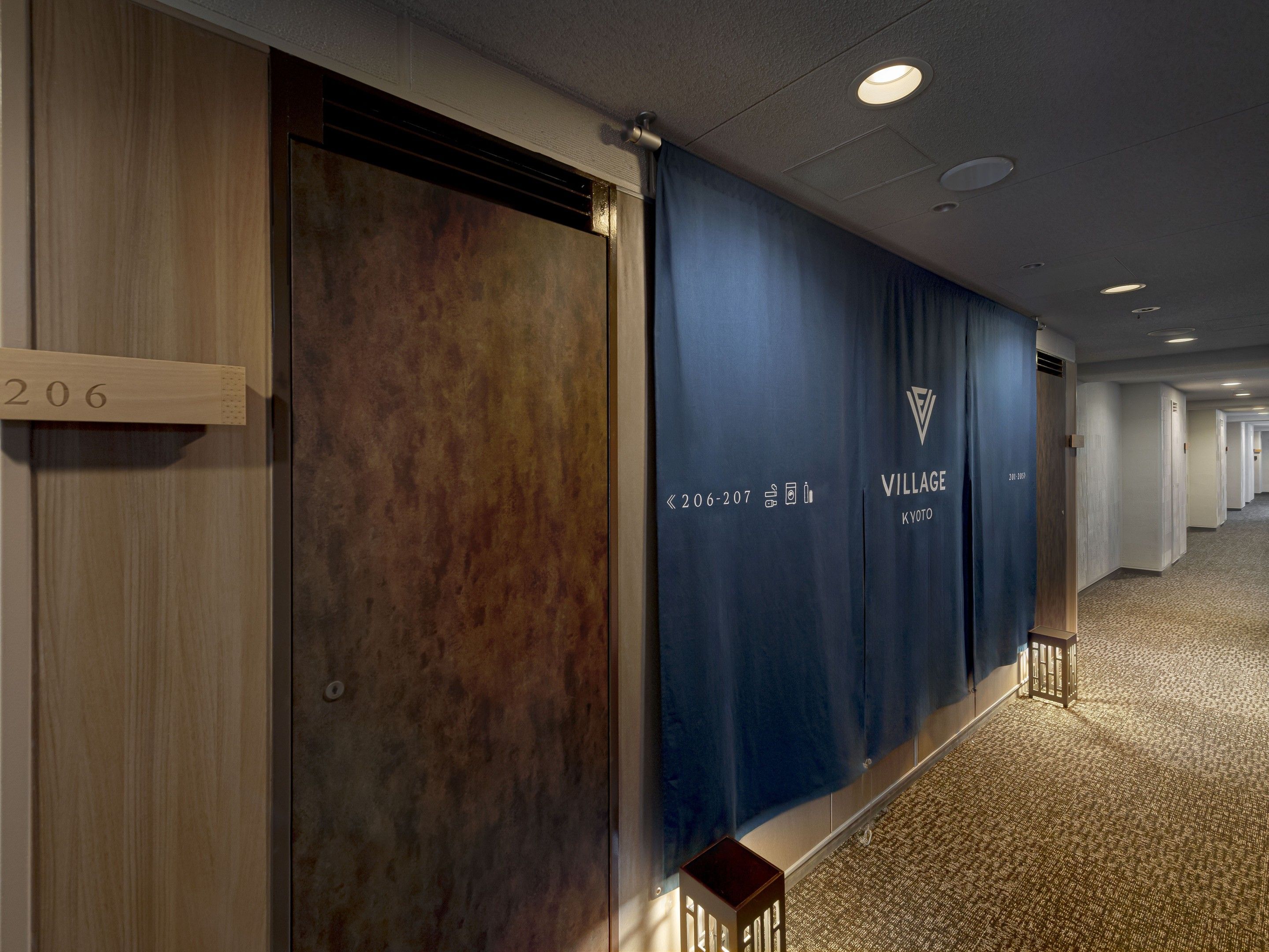 A hotel corridor with wooden paneling, a blue curtain, and a sign indicating room numbers 206-207.