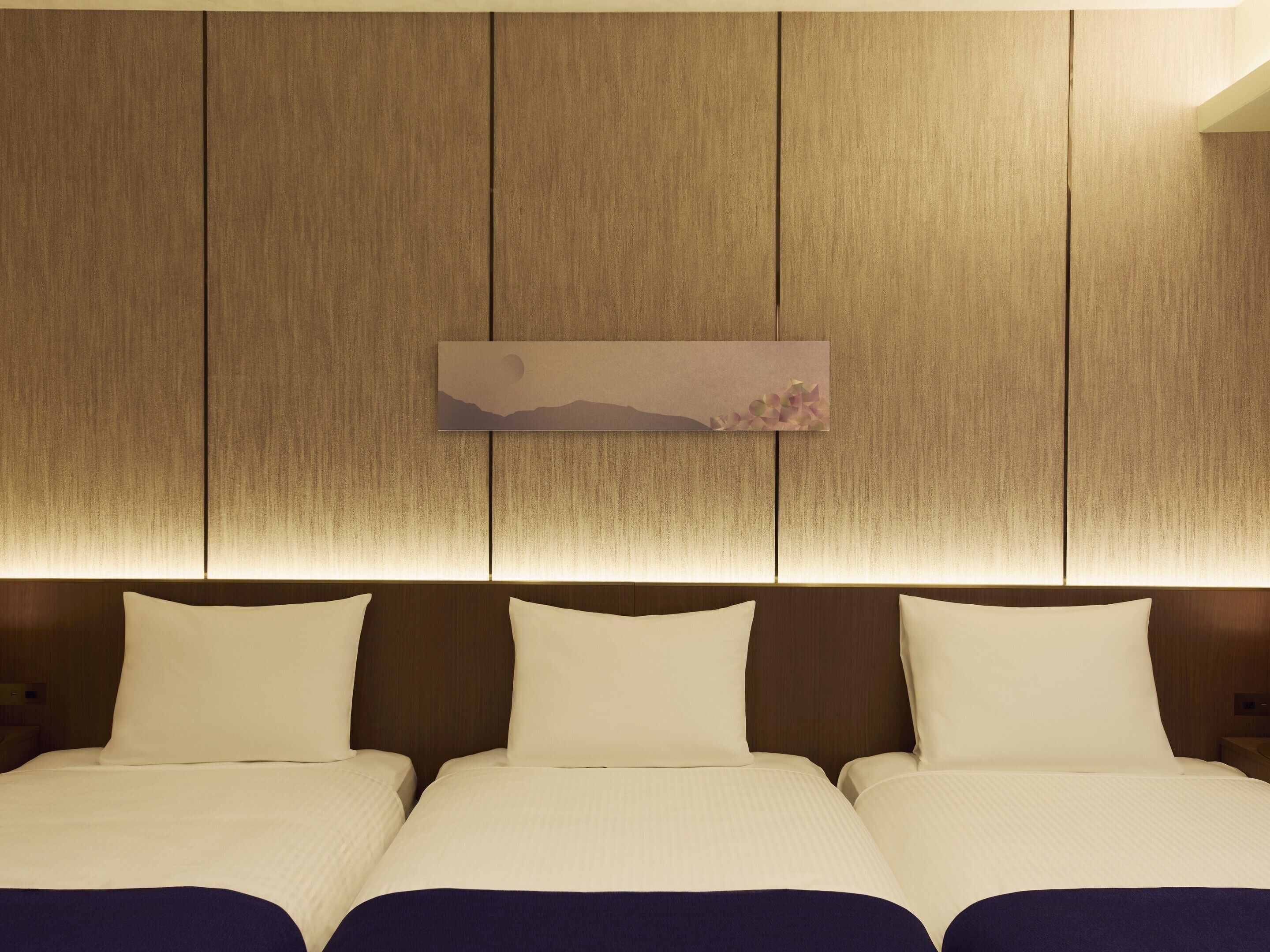 A hotel room with a large bed, a headboard with a wooden panel design, and a wall-mounted artwork depicting a landscape.