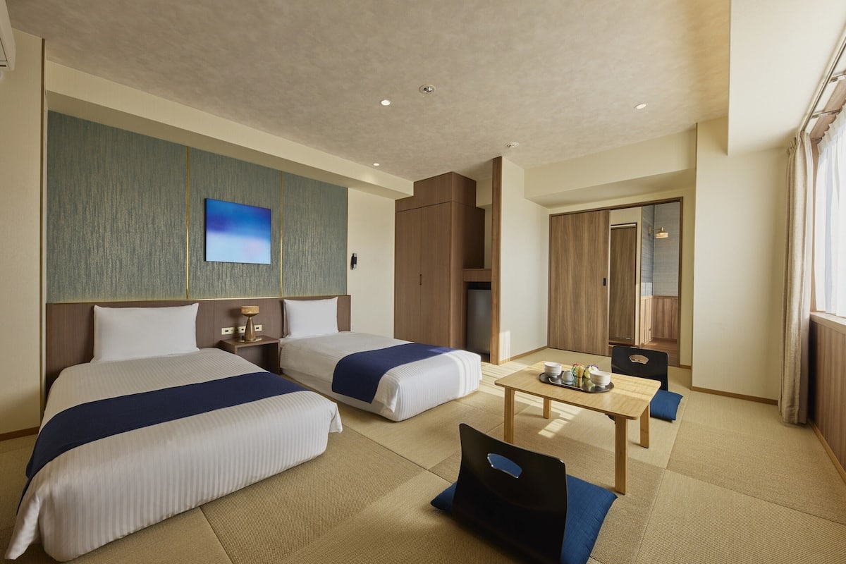 A hotel room with two beds, a small table with a tray of items, a mirror, and a wardrobe.