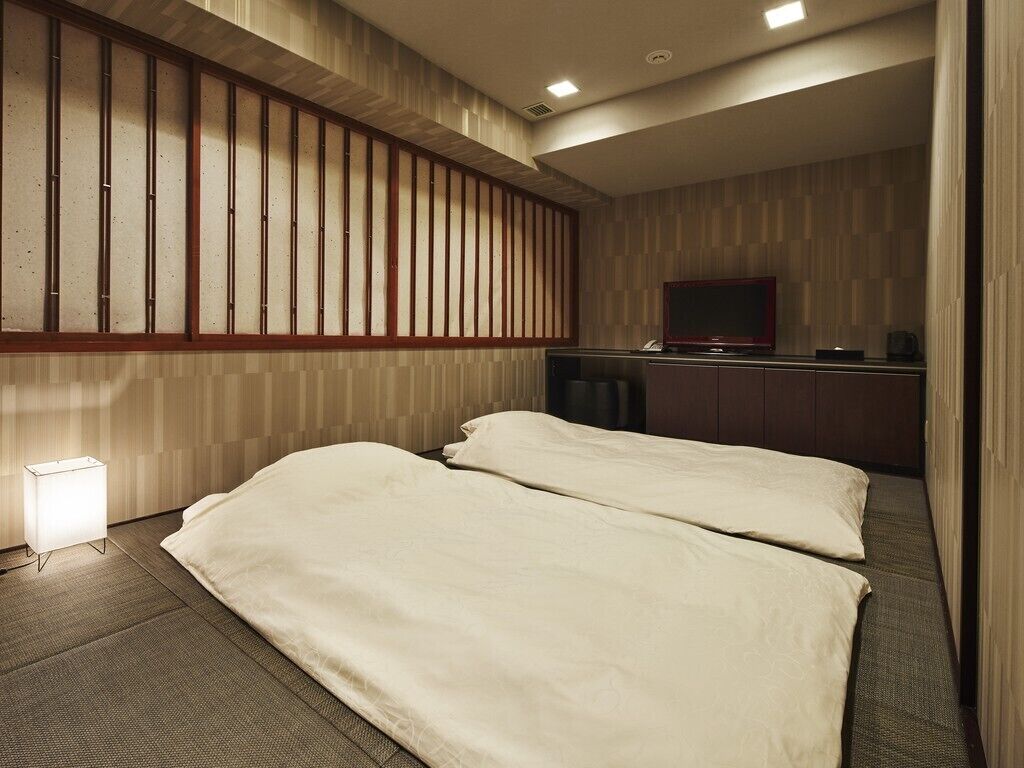 Quarto de hotel com duas camas, televisão, escrivaninha e abajur.