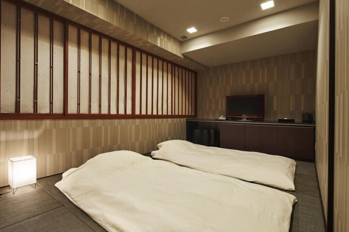 A hotel room with two beds, a TV, a desk, and a lamp.