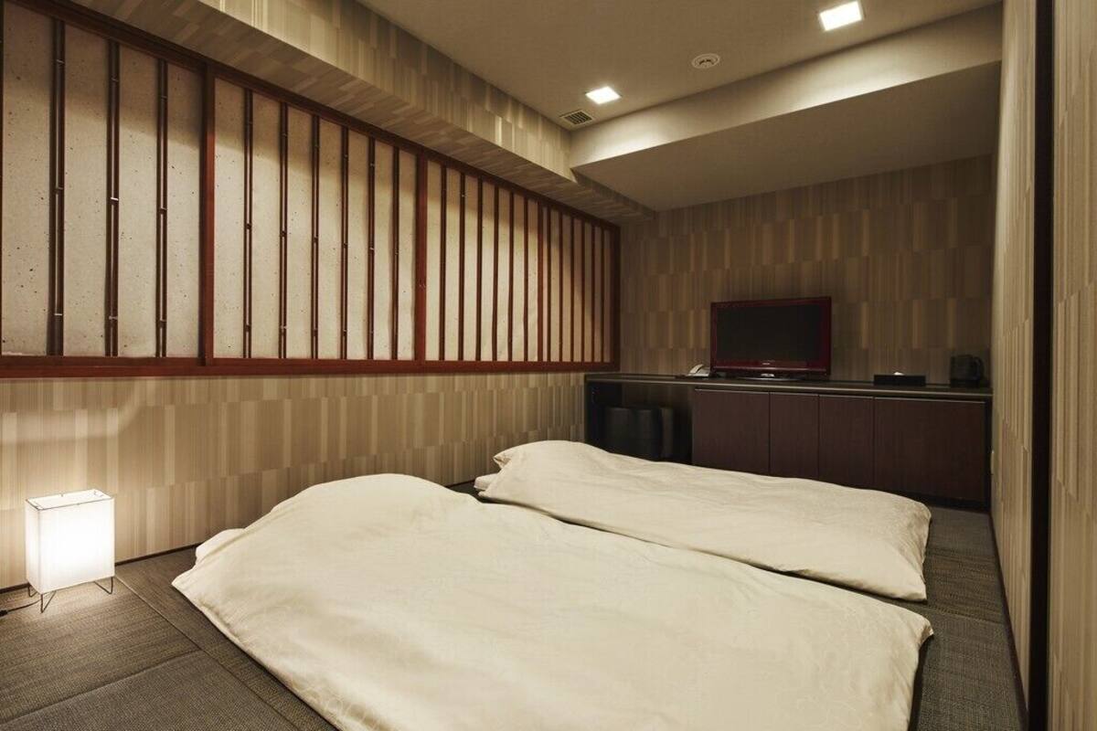 Quarto de hotel com duas camas, televisão, escrivaninha e abajur.